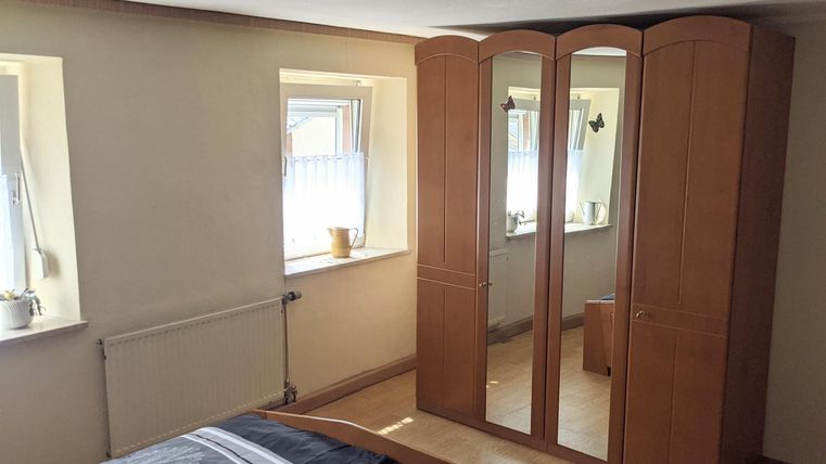 A bedroom with a large, bright wardrobe and two windows. The walls are in neutral colors and the floor is made of wood.