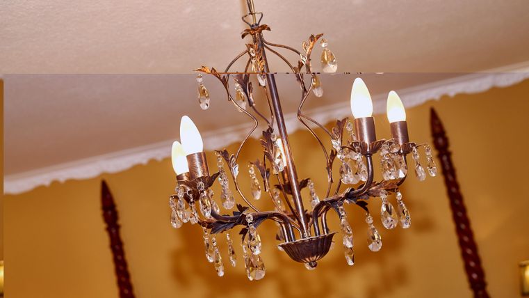 An elegant ceiling lamp with crystal pendants and multiple lights. It hangs in a room with yellow walls.