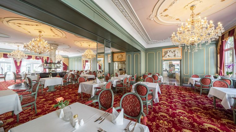 Een elegant restaurant met stijlvolle tafels en rode tapijten. Sprankelende kroonluchters verlichten de ruimte en creëren een gezellige sfeer.