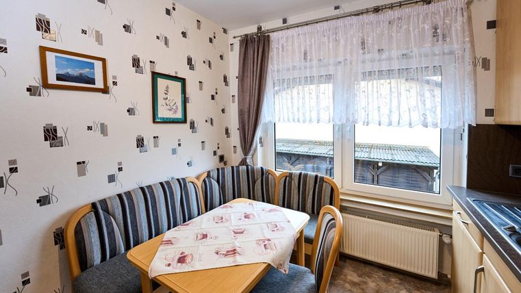 Eine gemütliche Küchenecke mit einem runden Tisch und gepolsterten Bänken. Die große Fensterfront lässt viel Tageslicht herein und bietet einen Blick nach draußen.