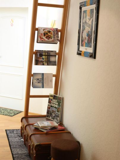 Ein einladender Flur mit einem Holzregal für Zeitschriften und einer dekorativen Leiter. Auf einem Hocker liegen einige Bücher und eine gemütliche Atmosphäre herrscht vor.