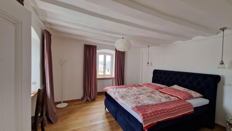 A bright bedroom with a blue bed and a beautiful bedding set. Large windows and stylish curtains create a pleasant atmosphere.