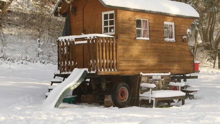 A cozy wooden cabin stands in a snow-covered landscape. In front of the cabin, there is a small staircase and a slide.