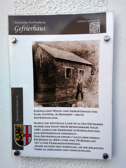 Ein historisches Schild über das Gefrierhaus in Karpfen, mit einer Schwarz-Weiß-Fotografie des Gebäudes und einer Person davor. Das Schild bietet Informationen über die Bedeutung und Geschichte des Ortes.