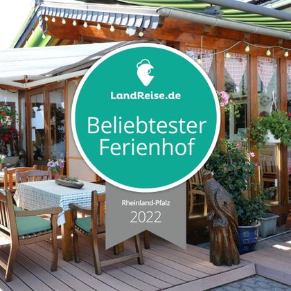 An inviting terrace with wooden furniture and many plants. The picture shows a certificate for the "most popular vacation farm" in Rhineland-Palatinate 2022.