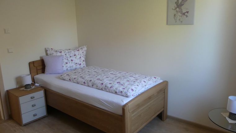 Ein einfaches Schlafzimmer mit einem Holzbett und bunten Bettwäsche. Neben dem Bett steht ein Nachttisch und an der Wand hängt ein Bild.