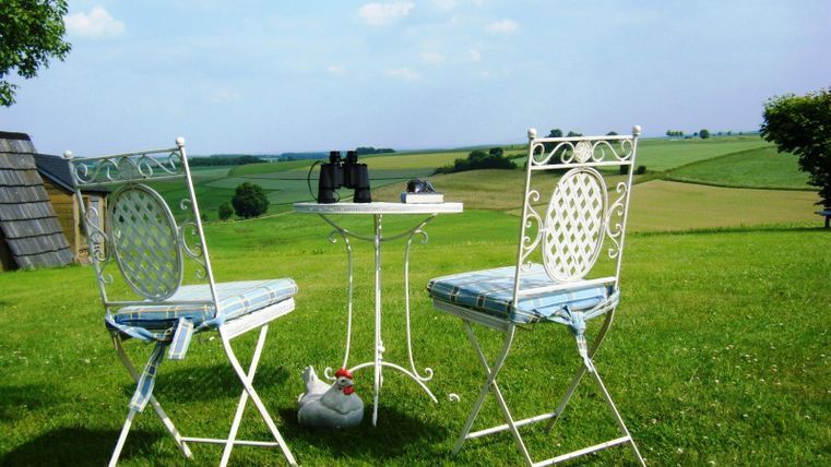 Een mooie tafel met twee stoelen buiten, omringd door een groene landschap. Op de tafel liggen een verrekijker en enkele boeken.