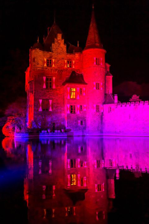 Ein beeindruckendes Schloss erstrahlt in bunten Lichtern bei Nacht. Das Licht wird im Wasser reflektiert und schafft eine magische Atmosphäre.