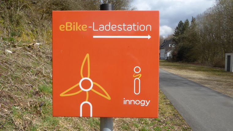 Een oranje aanwijzing voor een eBike-laadstation met een windkracht symbool. Het laadstation bevindt zich in de richting van de aangegeven pijl.