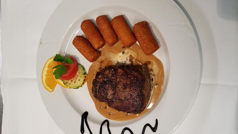 Ein leckerer Teller mit einem saftigen Steak, serviert mit Kroketten und einer Beilage aus Kartoffelpüree. Dazu gibt es eine Garnitur aus Salat und Zitrone.
