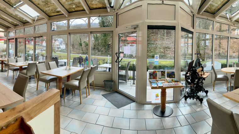 Ein helles und einladendes Restaurant mit großen Fenstern. Tische und Stühle sind ordentlich angeordnet und der Blick auf den Garten ist sichtbar.