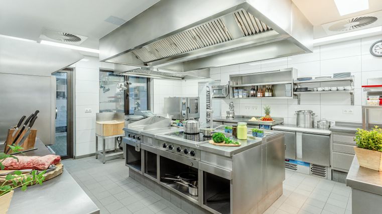 Moderne Profiküche mit Edelstahlgeräten und Arbeitsflächen, frischen Zutaten und Küchenutensilien.