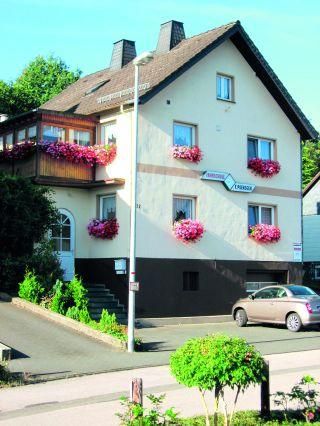 Ein charmantes Haus mit vielen bunten Blumenfenstern. Es hat eine helle Fassade und liegt an einer ruhigen Straße.