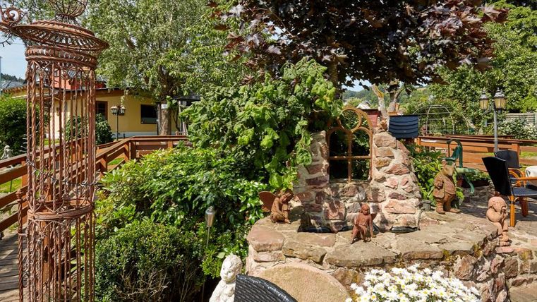 Ein schöner Außenbereich mit einem Steingarten und vielen Pflanzen. Im Hintergrund sind Sitzplätze und ein dekorativer Zaun zu sehen.