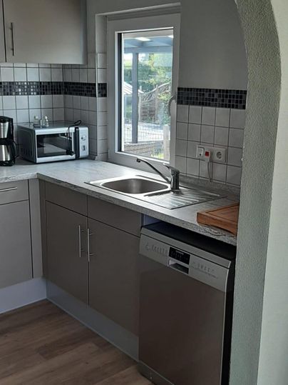 Eine moderne Küche mit einem Waschbecken, Geschirrspüler und Mikrowelle. Das Fenster lässt viel Tageslicht herein.