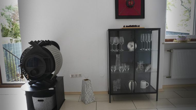 Ein moderner Raum mit einem stilvollen Design. Links befindet sich ein dekorativer Ventilator und rechts ein Glasregal mit Geschirr und Gläsern.