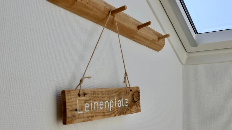Een houten bord met de tekst "Linnenplaats" hangt aan een muur. Boven hangt een kleine houten kledinghaak.