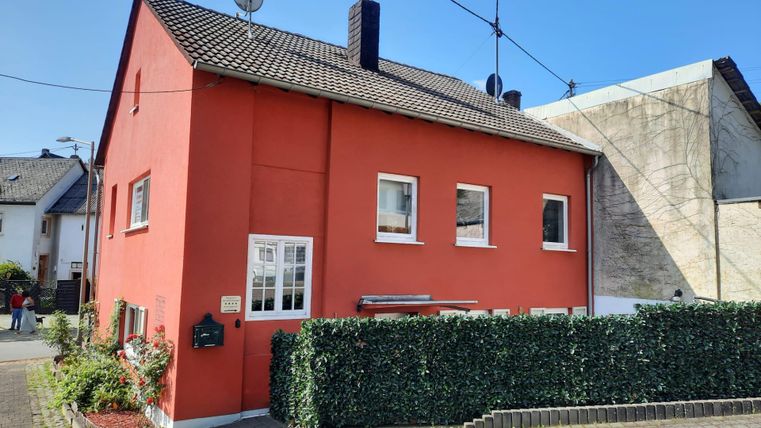 A red house with a planted front yard. It has bright windows and a clear blue sky in the background.