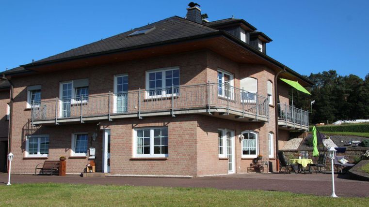 Ein modernes Haus mit einem großen Balkon und mehreren Fenstern. Der Garten ist gut gepflegt und lädt zum Entspannen ein.