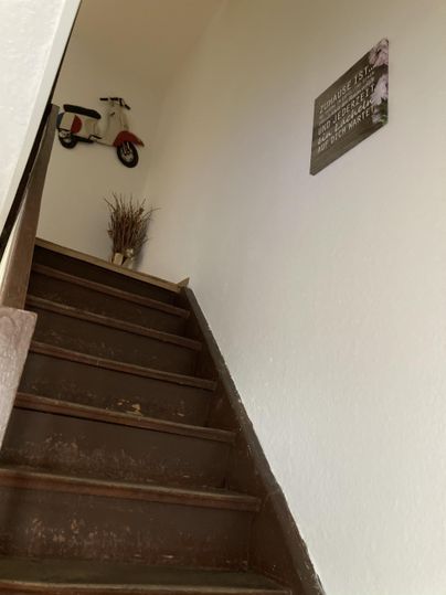 Een trap met houten treden leidt naar boven. Aan de muur hangt een klein motorfietsmodel en een decoratie.
