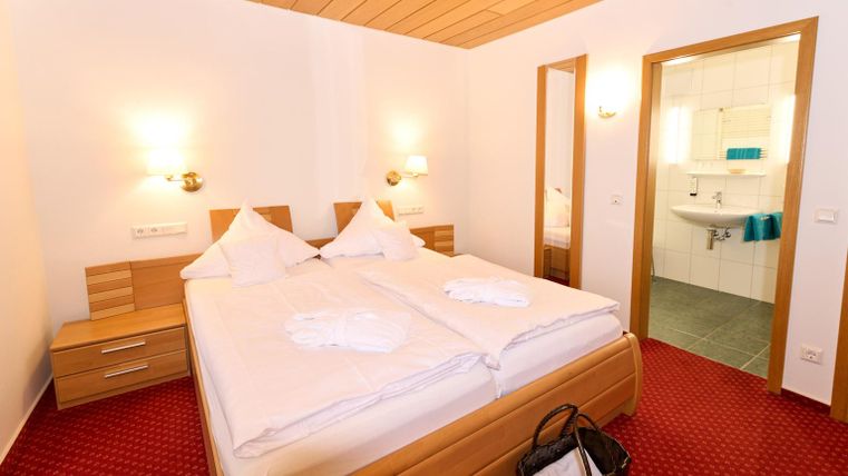 Een gezellige slaapkamer met een tweepersoonsbed en warme houten decoraties. De kamer beschikt over twee nachtkastjes en een aangrenzende badkamer.