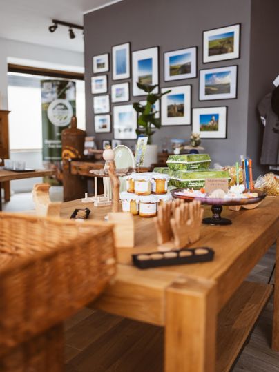 A store display with jars of jam, gift boxes, and pictures on the wall. A wooden table is laden with various products.
