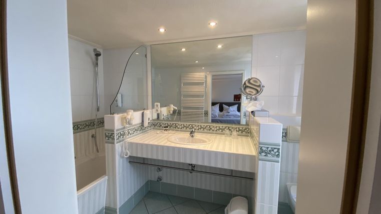 Ein modernes Badezimmer mit einem großen Spiegel und einer hellen, freundlichen Atmosphäre. Die Wände sind gefliest und es gibt eine Dusche sowie eine Badewanne.