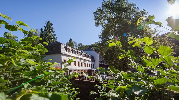 Ein malerisches Gebäude umgeben von grünen Pflanzen und Bäumen. Der klare Himmel sorgt für eine angenehme Atmosphäre.