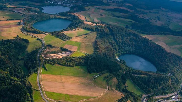 Een indrukwekkend landschap met twee blauwe meren en omringd door groene bossen en velden. De lucht is helder, wat de natuurlijke schoonheid van de regio benadrukt.