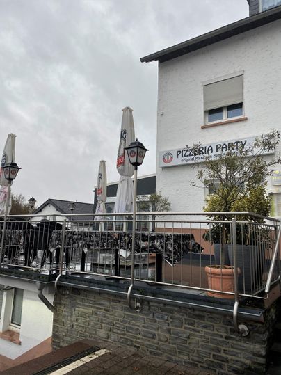 A restaurant named "Pizzeria Party" is visible. There is a terrace with umbrellas and tables.