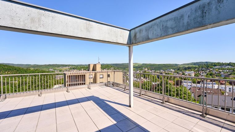 Eine großzügige Dachterrasse mit Blick auf die umliegende Landschaft und die Stadt. Der Himmel ist klar und blau, ideal für entspannte Stunden im Freien.