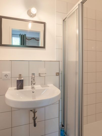 A modern bathroom with a white sink and a shower cubicle. There is a mirror hanging on the wall and there are bright tiles.