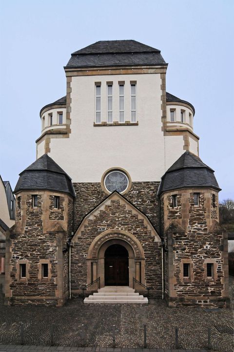 Eine historische Kirche mit einem markanten Eingang und zwei Turmähnlichen Strukturen auf beiden Seiten. Die Fassade kombiniert moderne und traditionelle architektonische Elemente.