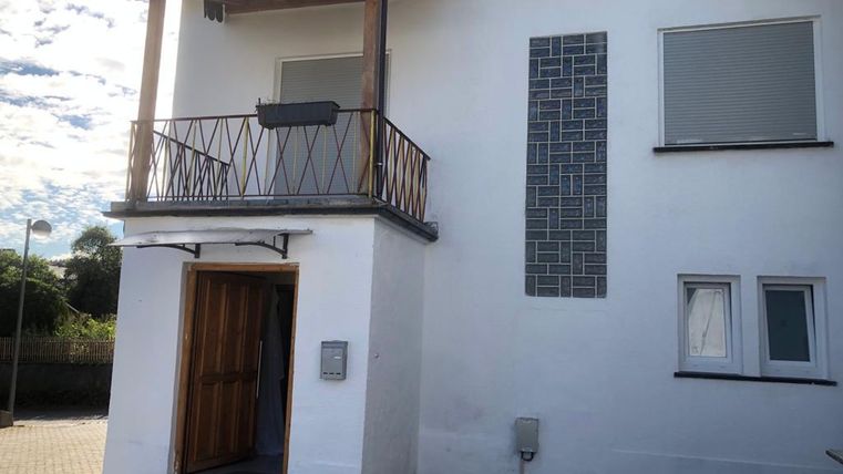 Ein modernes zweigeschossiges Haus mit einem Balkon. Die Fassade ist weiß und hat große Fenster.