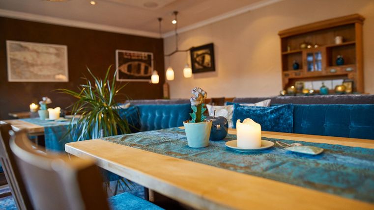 An inviting interior with a wooden dining table and blue upholstered benches. Soft light from lamps and candles creates a cozy atmosphere.