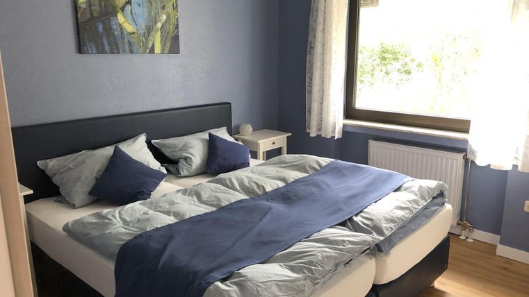 Een gezellige slaapkamer met een groot dubbelbed en blauwe beddengoed. De kamer heeft een raamfront met veel daglicht en een prachtig uitzicht.