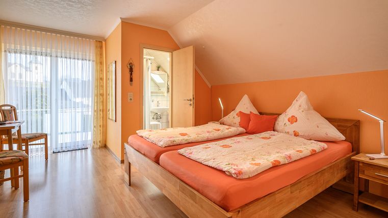 Ein gemütliches Schlafzimmer mit zwei Betten und bunten Bettdecken. Der Raum hat große Fenster mit Blick nach draußen und eine warme, einladende Farbgestaltung.