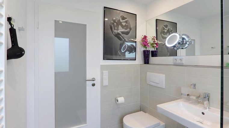 Een moderne badkamer met elegante kranen en een grote spiegel. Er zijn decoratieve planten en kunstwerken aan de muur.