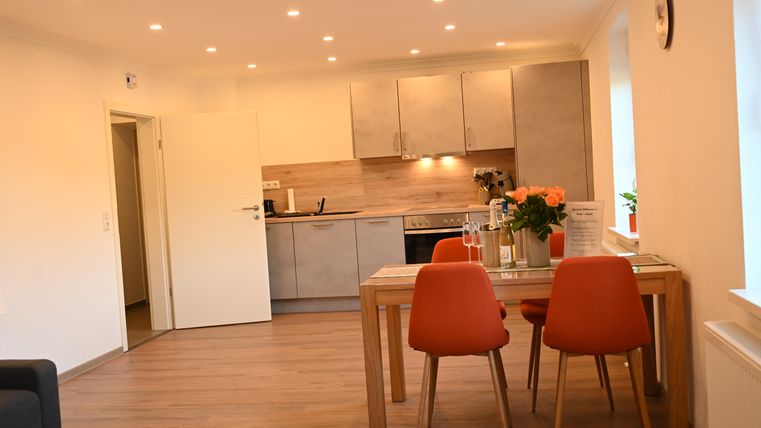 Een moderne, lichte keuken- en eetkamer met houten vloeren. De tafel is versierd met bloemen en er staan oranje stoelen.
