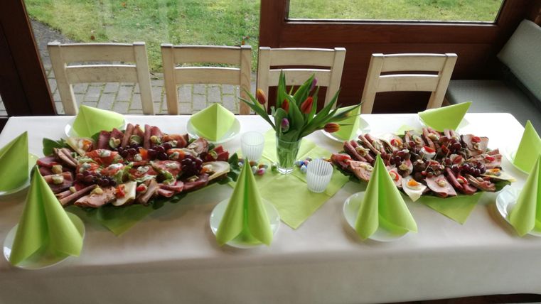 Ein festlich gedeckter Tisch mit verschiedenen Platten voller Köstlichkeiten. Tulpen in einer Vase und grüne Servietten ergänzen die Tischdekoration.
