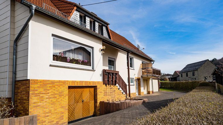 Ein helles Wohnhaus mit einem klaren Himmel im Hintergrund. Es hat eine gelbe Ziegelverkleidung und eine gemütliche Veranda.