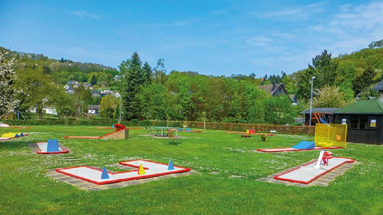 A mini golf course in a green park, surrounded by trees and hills. The players can play on various track layouts.