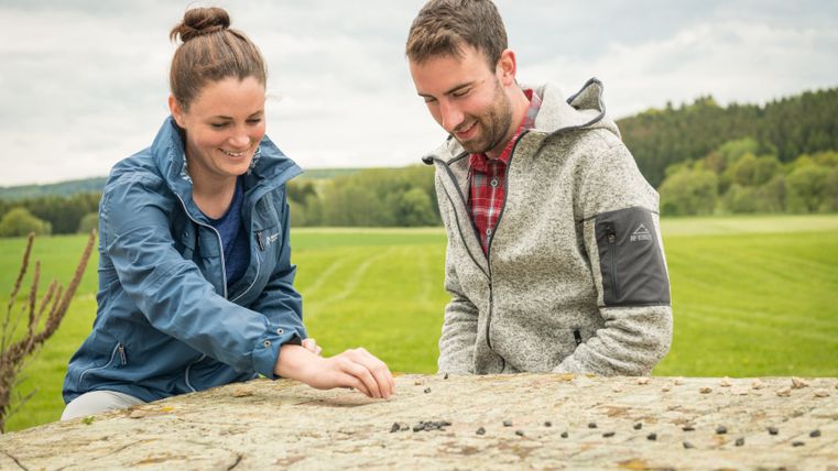 Zwei Personen spielen ein Spiel auf einem Stein im Freien.