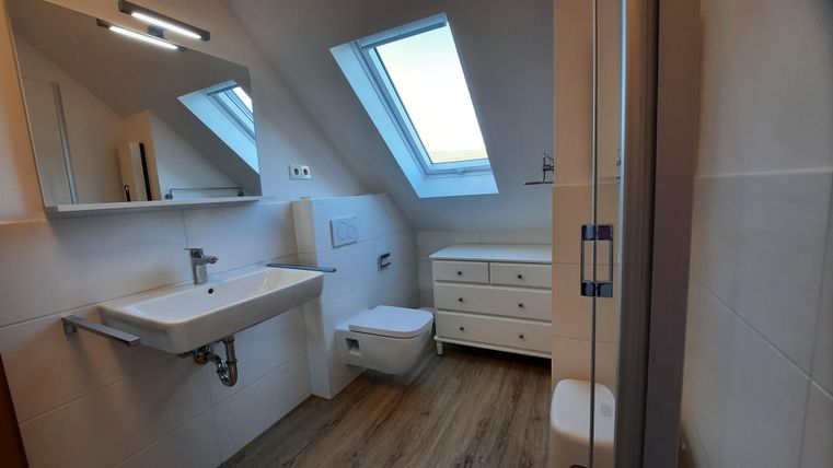A modern bathroom with a window and light wooden flooring. There is a sink, a toilet, and a cabinet.