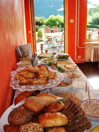 Ein reichhaltiges Frühstücksbuffet mit verschiedenen Brötchen, Croissants und frischem Obst. Die Umgebung ist hell und einladend mit Blick auf einen Garten.
