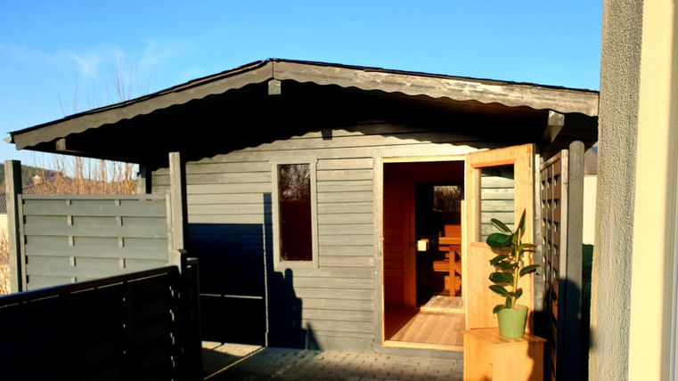 Een modern tuinhuis met een open deur en een kleine plantenpot erin. De lucht is helder en blauw, wat een uitnodigende sfeer creëert.