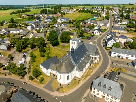 A picturesque overview of a small village with a church at its center. Surrounded by green fields and residential houses, the street portrays a tranquil rural atmosphere.