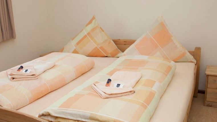 Ein gemütliches Schlafzimmer mit einem Doppelbett und zwei Kissen. Auf dem Bett liegen frisch gefaltete Handtücher.