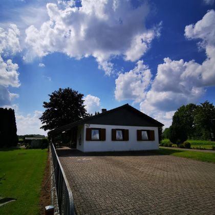 Een mooi vrijstaand huis met een grote oprit. De lucht is blauw en doorsneden met enkele mooie wolken.