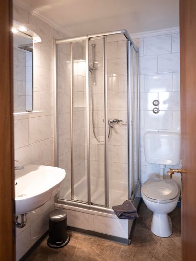 Ein modernes Badezimmer mit einer Dusche, einem Waschbecken und einer Toilette. Die Wände sind mit hellen Fliesen bedeckt.